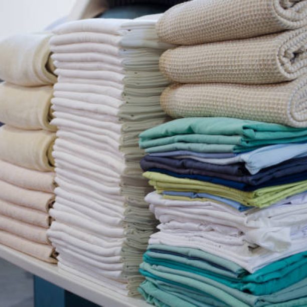Stack of folded clean sheets, surgical clothes  and industrial iron in an industrial laundry. Cleaning and ironing service for hospitals and clinics. Selective focus.